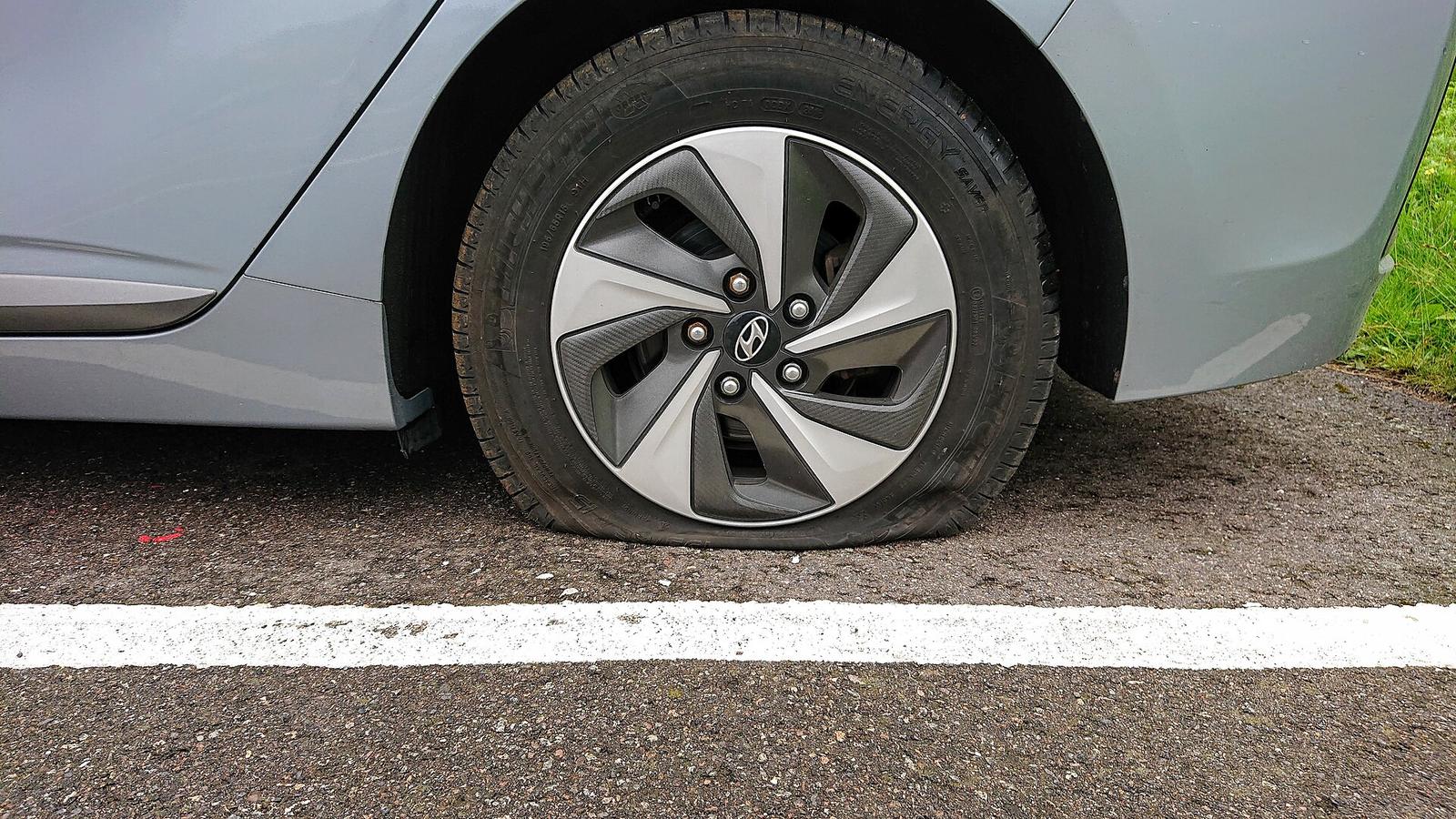 A flat tire on a silver car parked at the edge of the road